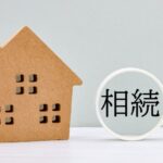 ミニチュアの家模型と虫眼鏡の中に相続の文字